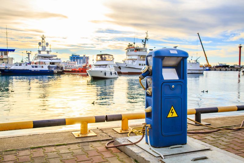 Charging station for boats, electrical outlets to charge ships in harbor - supply electricity for recharging of battery on shore in marina jetty. Electrical power sockets bollard point on pier near sea coast. Luxury yachts docked in port at sunset.