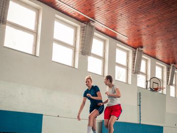 Two women playing basketball indoors in a gymnasium.