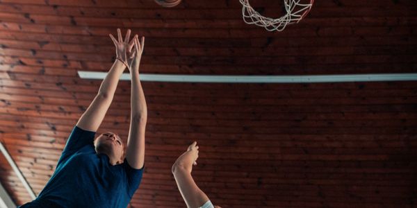 Two basketball players reaching for the ball near the hoop.