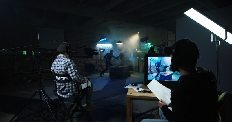 Director watching actors playing fight scene while shooting movie on stage set