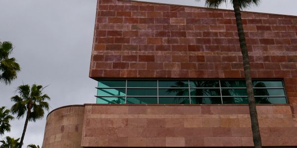 Modern building with red stone facade and large glass windows under an overcast sky.
