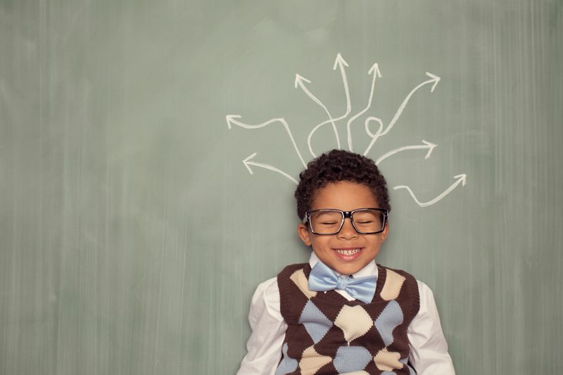 A young retro nerd boy is sitting against a chalkboard laughing while many arrows of possibilities are coming from his head. He is a smart child excited to try new things and explore his possibilities.
