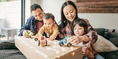 Family playing with wooden toy cars on a DIY race track at home.