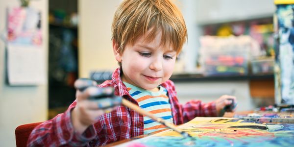 Young boy happily painting with bright colors indoors.