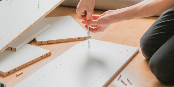 Person assembling furniture using a screwdriver on wooden floor.