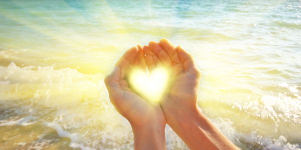 Hands holding a glowing heart by the beach.