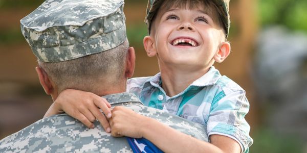 A joyful child hugs a soldier holding an American flag.