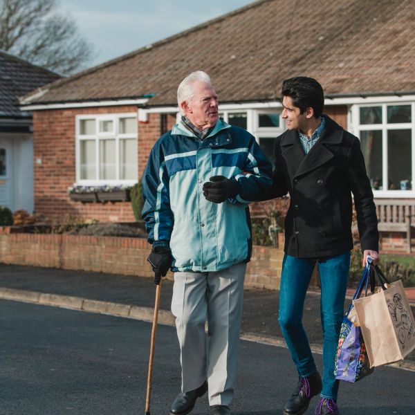 Young man helping elderly man walk outside.
