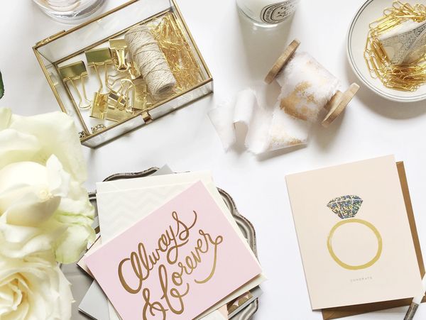 Elegant wedding cards, gold accessories, and white roses on a clean white surface.