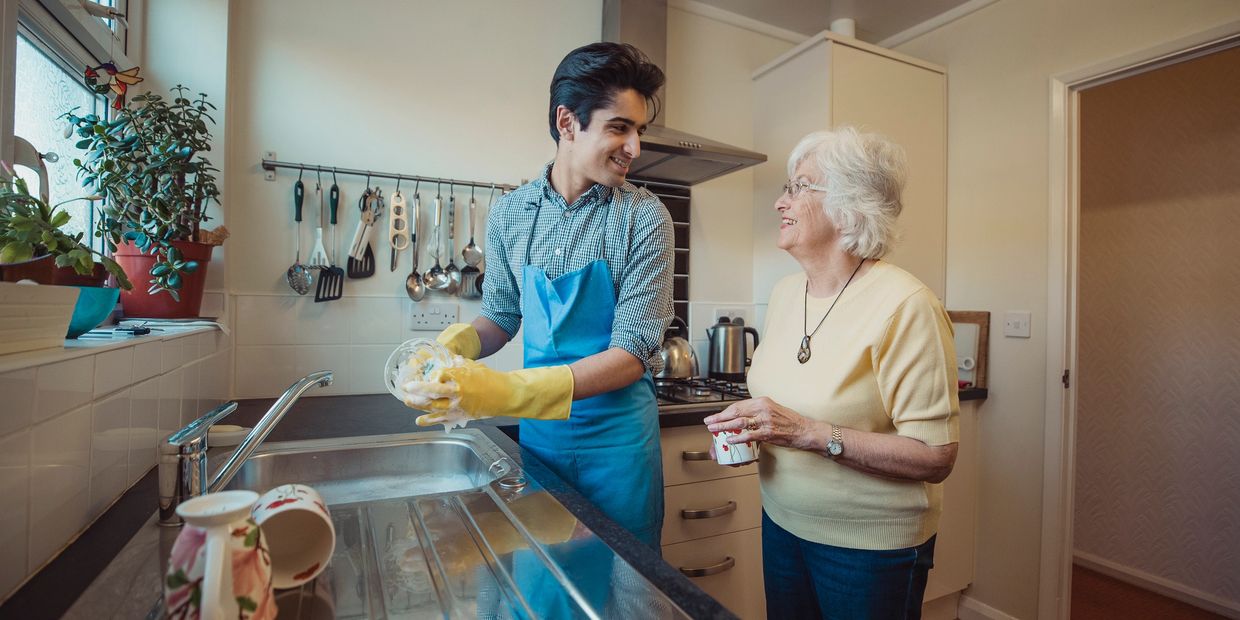 Support worker washing dishes for elderly lady 