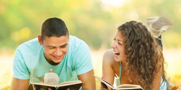 Two young people laughing and reading books outdoors.