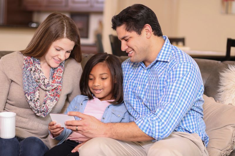 Multi-ethnic family members at home using cell phone.  Mixed race young couple with adopted or foster care child.