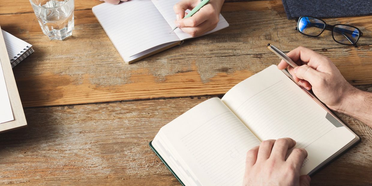 A person writing in a notebook on top of a table.