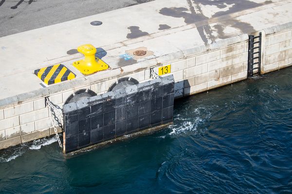 Harbor dock with yellow bollard, black rubber fender, and ladder by deep blue water.