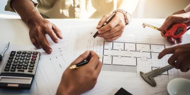 People working on architectural plans with tools and calculator.