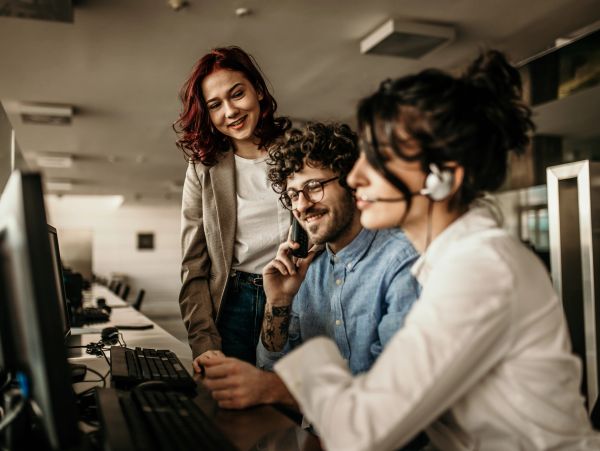 Three coworkers collaborating at a desk with computers.