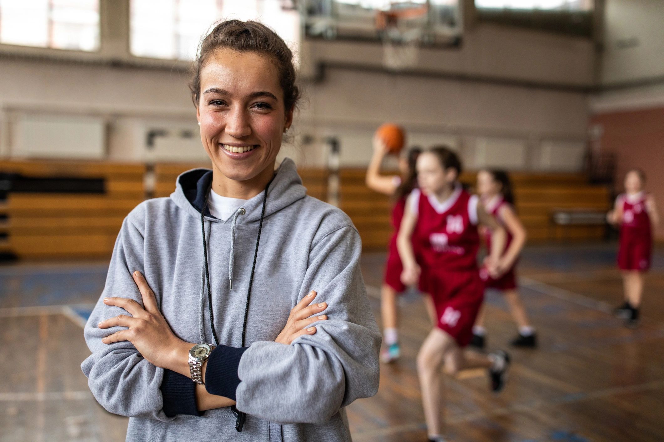 Smiling female basketball coach with arms crossed in gym.