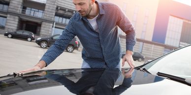 Man polishing car hood outdoors in daylight.