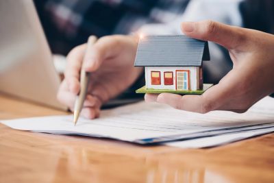 Person holding miniature house model while signing document.