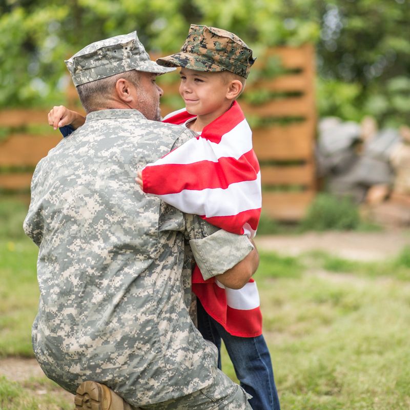Happy family reunited father soldier and his son holding american flag outdoors tender scene