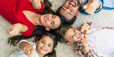 A happy family lying on the floor, smiling and pointing at the camera.
