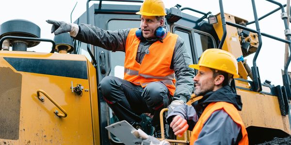 Construction workers discussing plans beside heavy machinery.