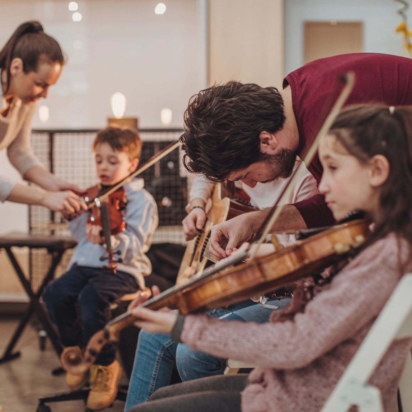 An adult teaching children to play violin and guitar.