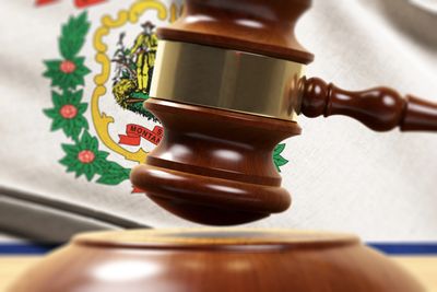 Wooden judge's gavel with West Virginia state flag in background.