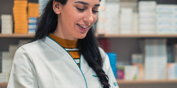 Pharmacist in white coat writing on clipboard in a pharmacy.