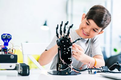 A boy happily assembles a robotic hand in a bright room.