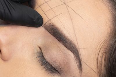 Close-up of eyebrow shaping with guiding lines on forehead.