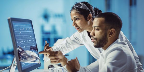 Two scientists analyze data on a computer screen in a lab.