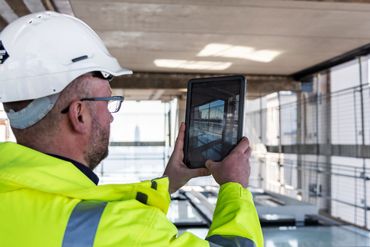 Construction worker in safety gear using a tablet on-site.