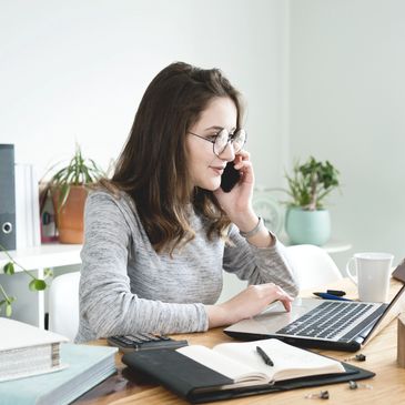 Woman talking on phone while working on laptop.