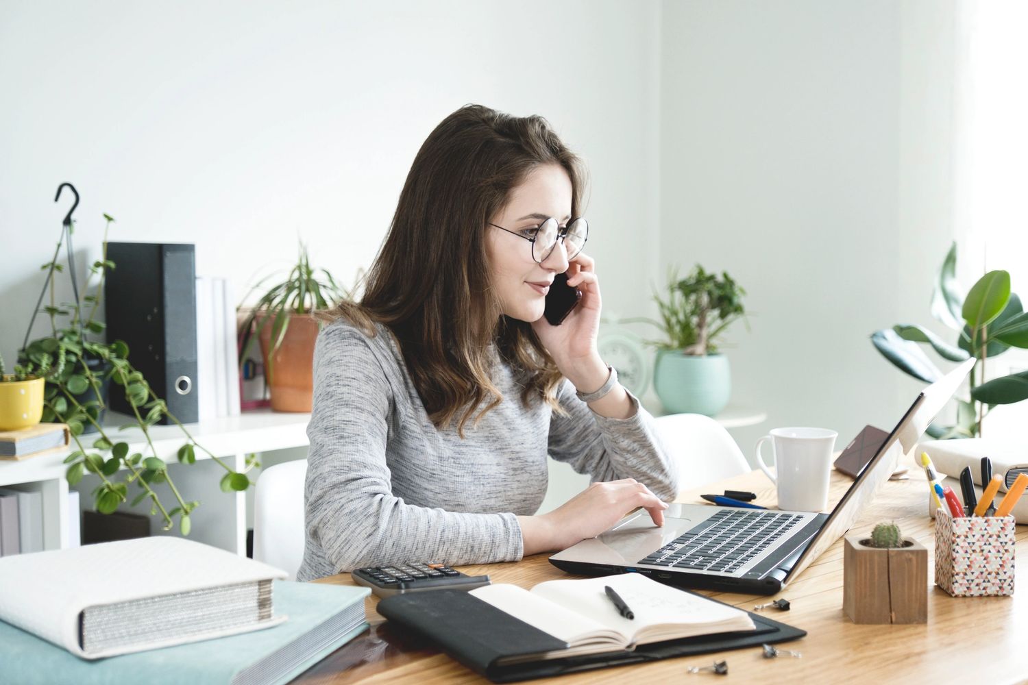 Young woman working on laptop and talking on phone at home office.