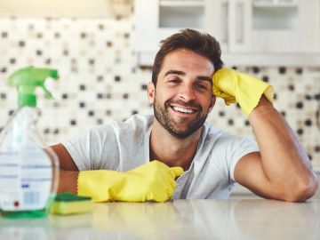 Smiling man wearing yellow gloves cleaning a kitchen counter.