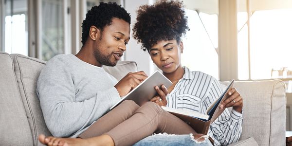 Couple using tablet and reading book on couch.