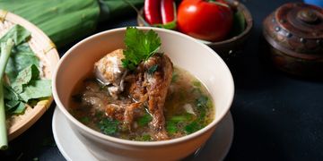 A bowl of chicken soup garnished with fresh herbs and vegetables.