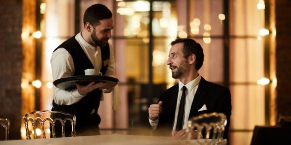 Waiter serving coffee to a seated man in a restaurant.