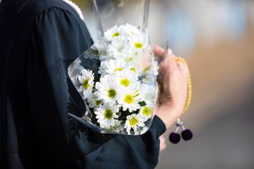 Person holding a bouquet of white daisies wrapped in plastic.