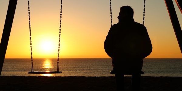 A person sits alone on a swing at sunset by the ocean.