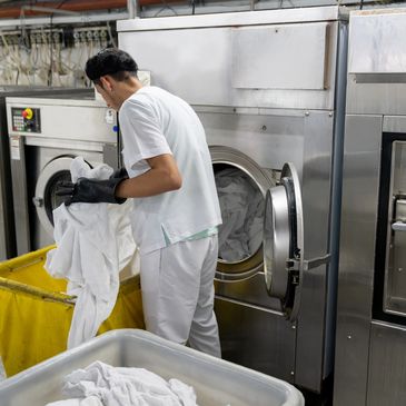 A person loads white laundry into an industrial washing machine in a laundry facility.