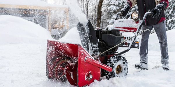 Person using a red snow blower to clear snow from driveway.