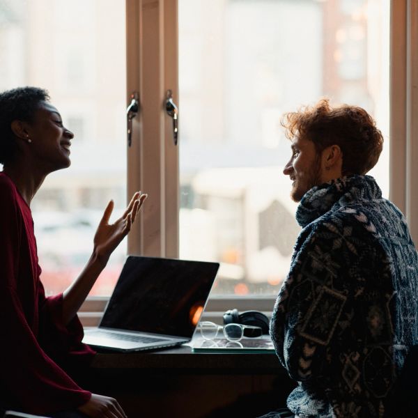 Two people chatting by a window with a laptop.