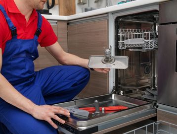 Technician repairing a dishwasher with tools inside the door.