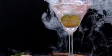 A cocktail glass with smoke and a garnish inside.