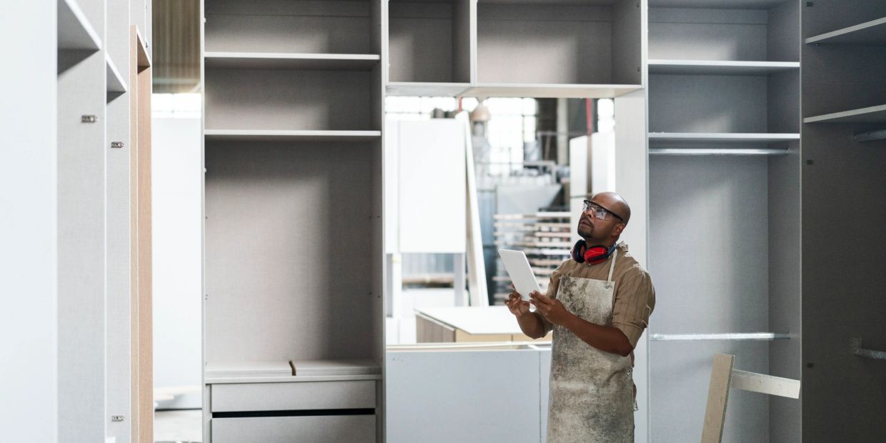 Carpenter inspecting a large shelving unit in a workshop with a tablet.