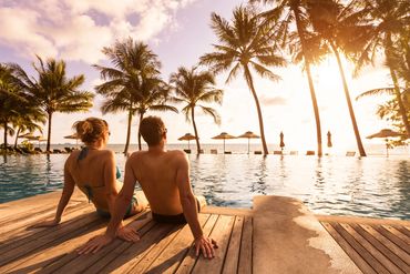 Couple sitting at edge of pool looking at palm trees