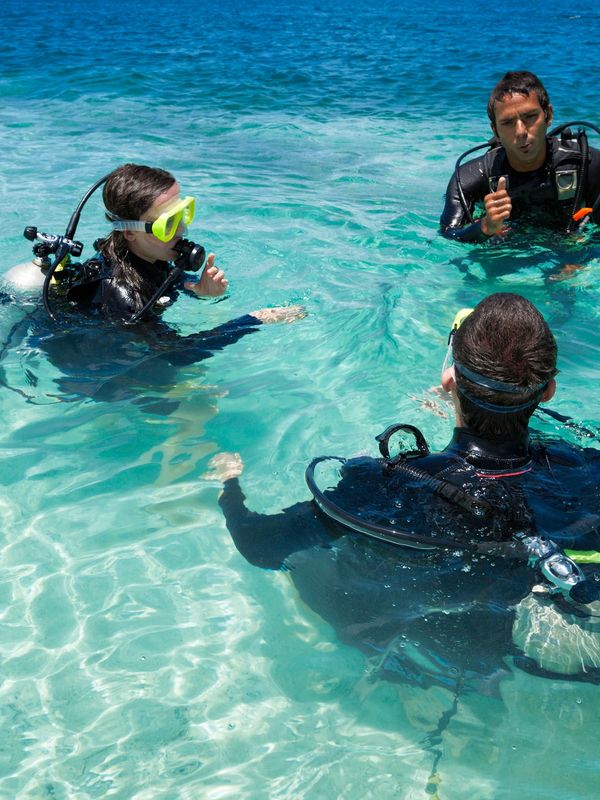Three scuba divers in clear blue water, preparing or discussing their dive.