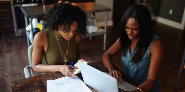Two women working together at a table with a laptop and papers.